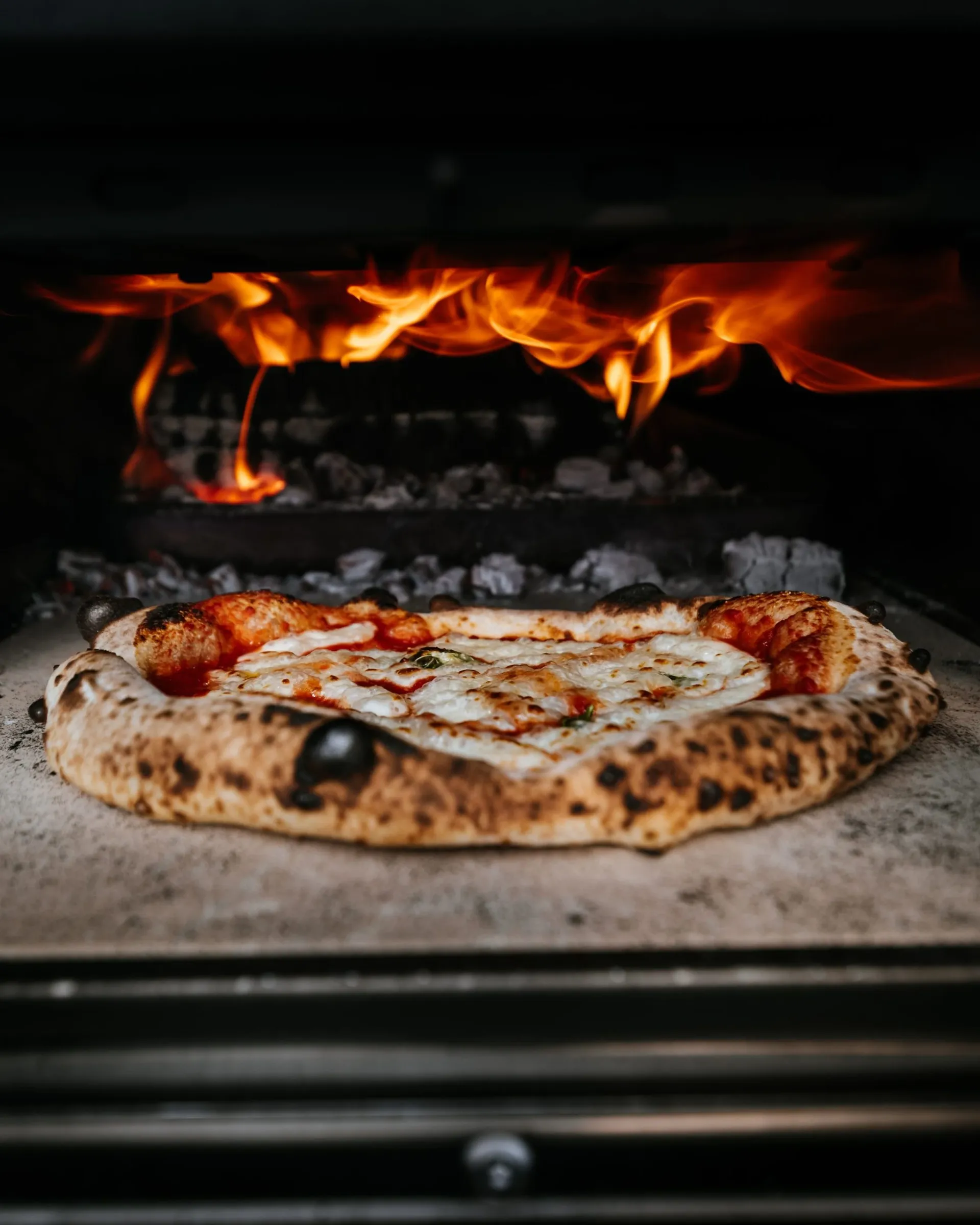 Une pizza cuit au fond d'un four à bois, devant les flammes