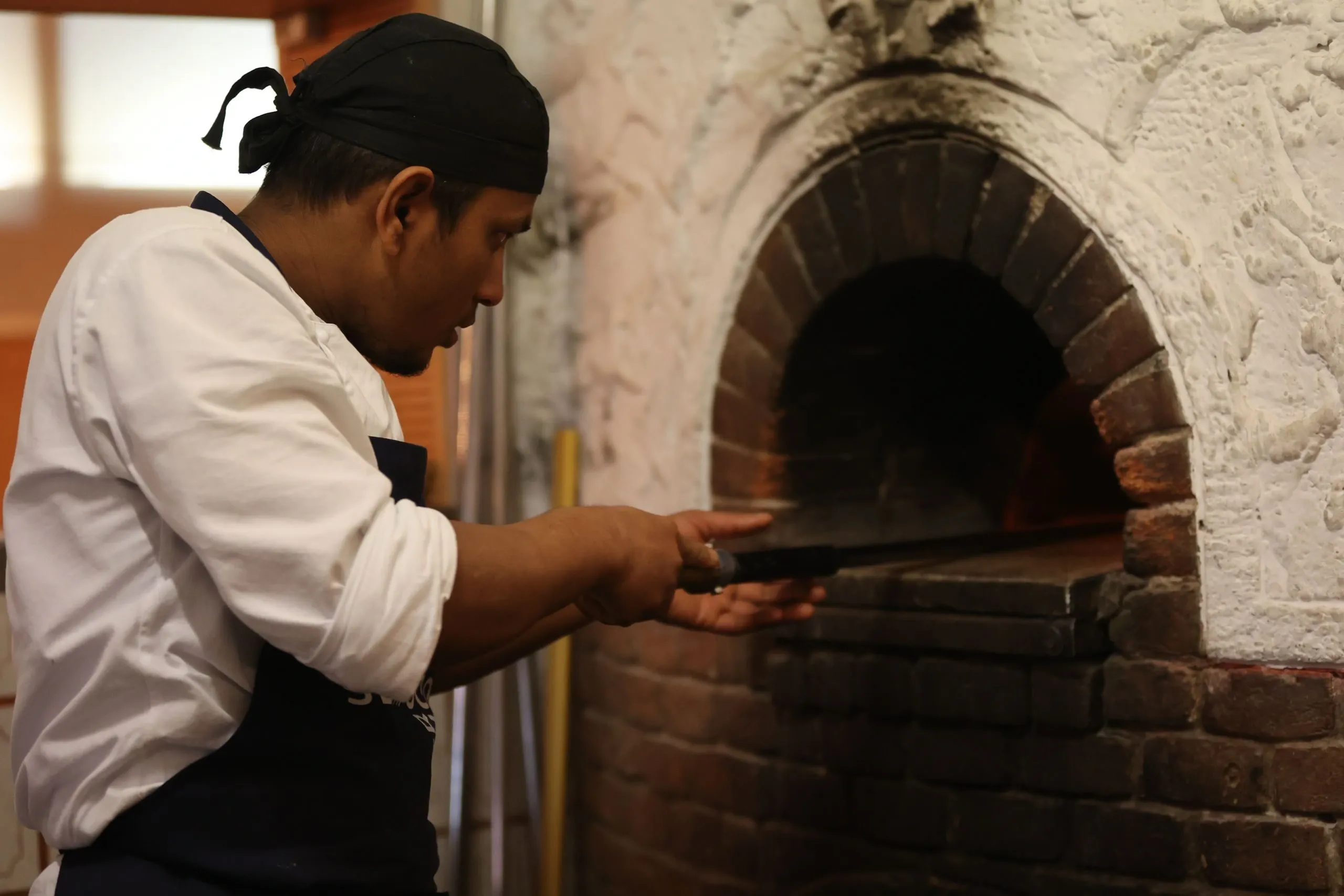 Marco enfourne une pizza dans le four en briques