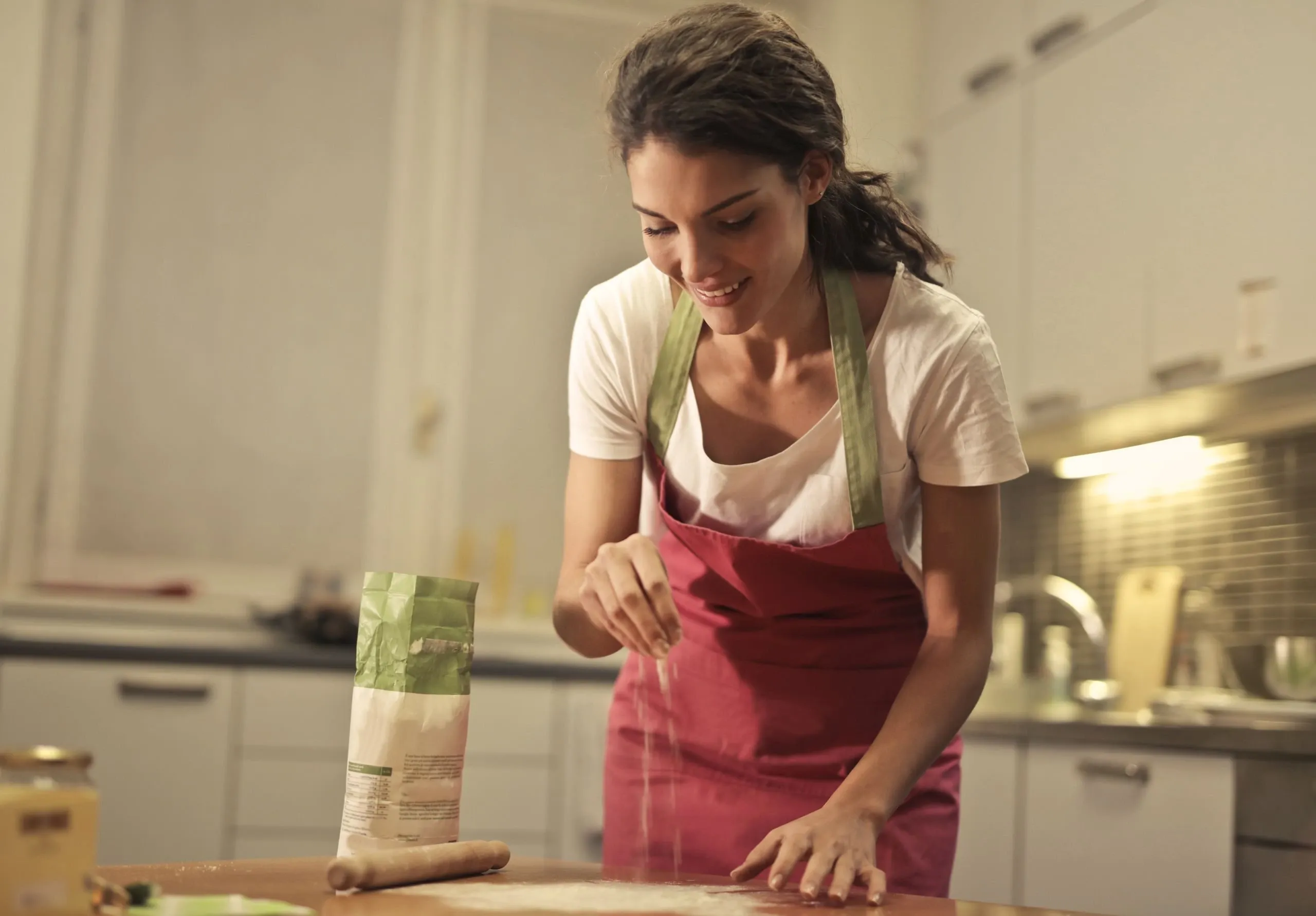 Giulia, en tablier rouge, saupoudre la pâte de farine en souriant